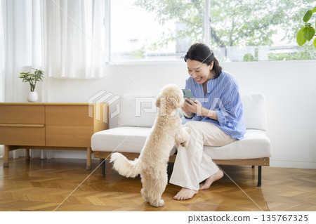 A middle-aged woman taking a photo of her beloved dog with her smartphone. Image of life with a dog. 135767325