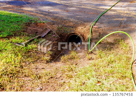 Water flows from cleaning drainage trench to dirt path, with shovel green hose Water flows from cleaning drainage trench to dirt path, with shovel green hose 135767458