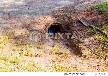Drainage pipe sits on abstersion trench dirt road water flows out from pipe into surrounding area. 135767461
