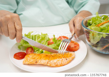 Asian elderly woman patient eating salmon stake and vegetable salad for healthy food in hospital. Asian elderly woman patient eating salmon stake and vegetable salad for healthy food in hospital. 135767748