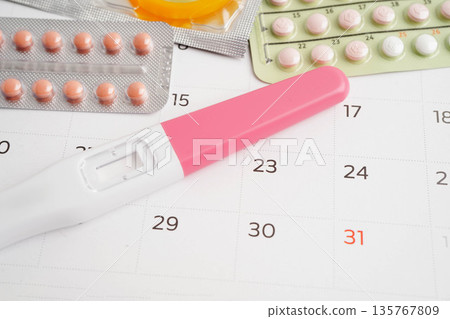 Pregnancy test with birth control pills and condom for female on calendar, ovulation day. 135767809