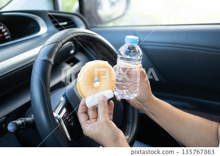 Asian woman driver hold and eat hamburger in car, dangerous and risk an accident. 135767863