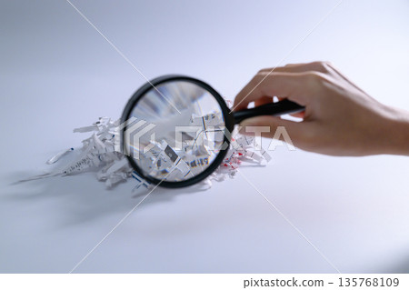 Hand examining shredded paper with a magnifying glass 135768109