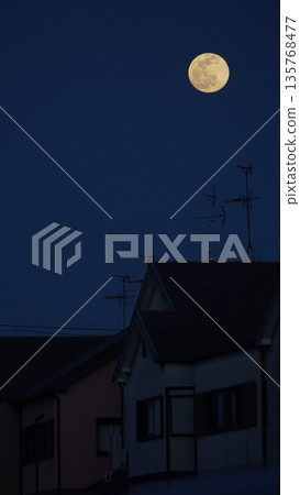 A large full moon rises as if watching over a residential area at night A large full moon rises as if watching over a residential area at night 135768477