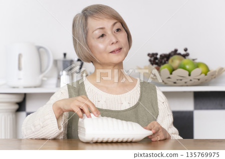 Senior woman pouring hot water into a hot water bottle in the kitchen Senior woman pouring hot water into a hot water bottle in the kitchen 135769975