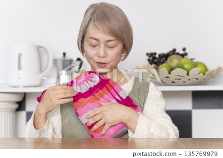 廚房裡,一位老婦人正往熱水袋裡倒熱水。 廚房裡,一位老婦人正往熱水袋裡倒熱水。 135769979