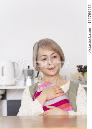 廚房裡，一位老婦人正往熱水袋裡倒熱水。 135769983