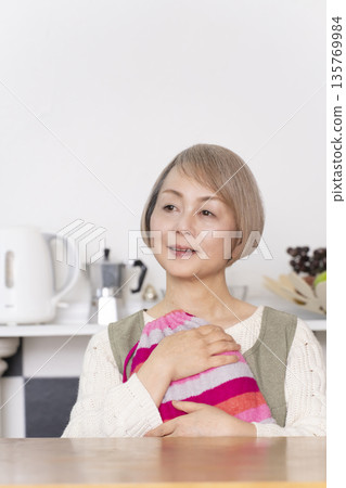 Senior woman pouring hot water into a hot water bottle in the kitchen 135769984