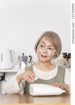 Senior woman pouring hot water into a hot water bottle in the kitchen 135769990