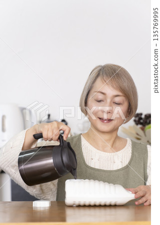 廚房裡,一位老婦人正往熱水袋裡倒熱水。 廚房裡,一位老婦人正往熱水袋裡倒熱水。 135769995