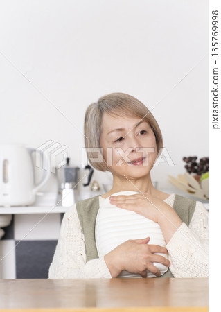 Senior woman pouring hot water into a hot water bottle in the kitchen 135769998