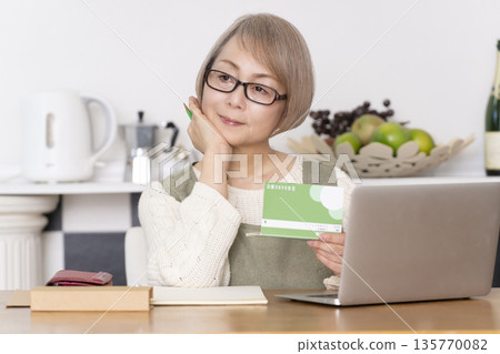 Senior woman keeping household accounts in the kitchen Senior woman keeping household accounts in the kitchen 135770082