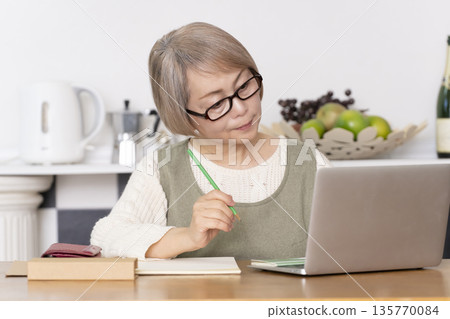 Senior woman keeping household accounts in the kitchen Senior woman keeping household accounts in the kitchen 135770084