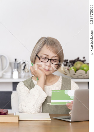 Senior woman keeping household accounts in the kitchen Senior woman keeping household accounts in the kitchen 135770093