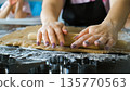 Close-up of a mother rolling ginger cookie dough on a floured surface while her daughters watch, warm family interaction moment 135770563