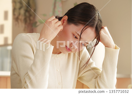 A young woman holding her head with an anxious expression 135771032