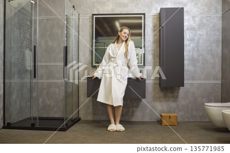 Smiling young woman in bathrobe standing in bathroom, enjoying freshness after shower at home. 135771985