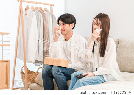 一對年輕的亞洲夫婦在家裡的客廳沙發上看電視，兩人（親密互動，流淚，淚流滿面） 135772509