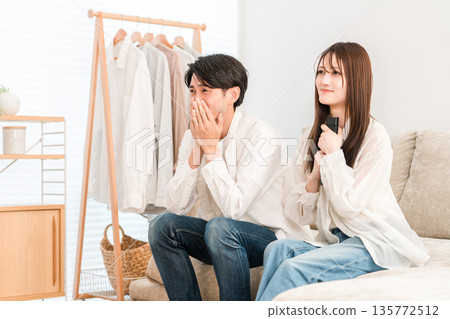 一對年輕的亞洲夫婦在家裡的客廳沙發上看電視，兩人（親密互動，流淚，淚流滿面） 135772512