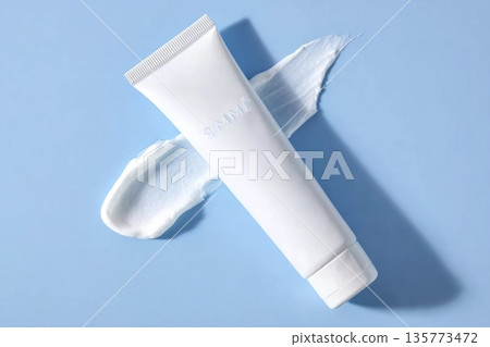 A smooth skincare cream dollop beside a white cosmetic tube on a soft blue background, showcasing texture and packaging A smooth skincare cream dollop beside a white cosmetic tube on a soft blue background, showcasing texture and packaging 135773472