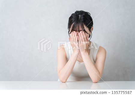 一位身穿背心的年輕亞裔女子哭泣，可能是因為壓力或驚嚇而感到擔憂。 135775587