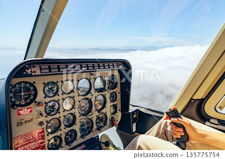 Man pilot operating helicopter control panel and joystick during flight, high above clouds. Luxury Cape Town tour. Aircraft cockpit view. Man pilot operating helicopter control panel and joystick during flight, high above clouds. Luxury Cape Town tour. Aircraft cockpit view. 135775754