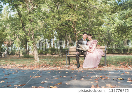 Couple taking wedding photos on a park bench 135776775