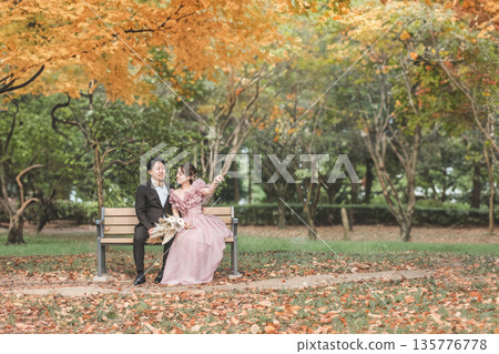 一對新人在公園長椅上拍攝婚紗照。 135776778