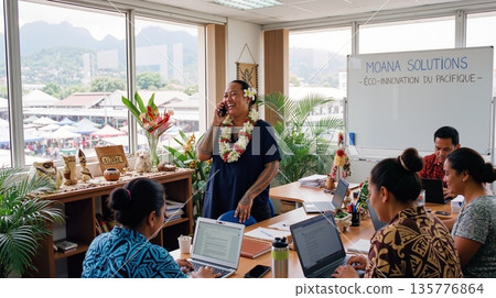 Tahitian female entrepreneur wearing a flower lei on phone call in office with team working on laptops 135776864
