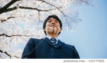 A male student with a hopeful expression against the backdrop of blue sky and cherry blossoms 135777005