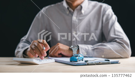 Man calculates car loan finance, preparing auto contract document for purchase, dealership sale with insurance details on clipboard, small blue car model rests on paperwork Man calculates car loan finance, preparing auto contract document for purchase, dealership sale with insurance details on clipboard, small blue car model rests on paperwork 135777462