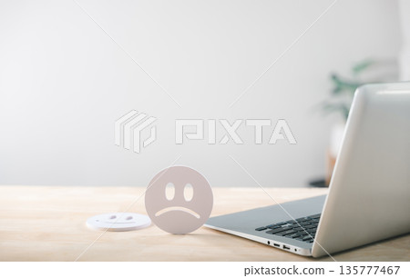 Sad face icon shows emotional contrast representing unhappy customer survey feedback with happy symbol nearby on desk with laptop for online service review 135777467