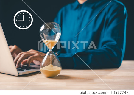 Hourglass time glass sand clock displays business urgency concept, timer for optimize growth, person works on laptop for important deadline countdown Hourglass time glass sand clock displays business urgency concept, timer for optimize growth, person works on laptop for important deadline countdown 135777483
