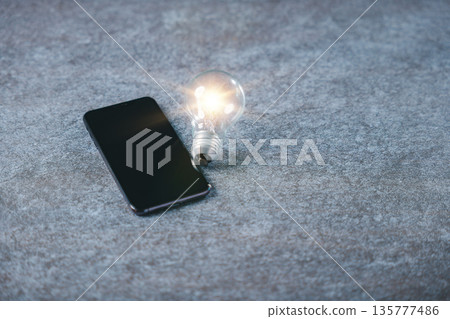 Glowing light bulb sparks digital marketing business idea innovation, creative knowledge development for market concept helps strategy beside smartphone on grey textured background 135777486