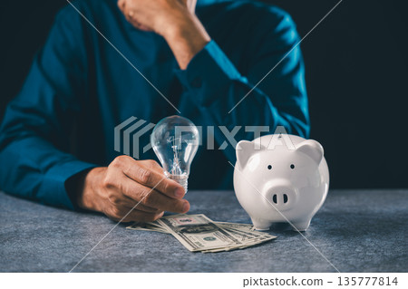 Knowledge fuels financial innovation while businessman holds lightbulb near white piggy bank with money, creating bright business idea concept for smart wealth and research goals 135777814