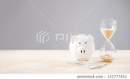 Money savings concept with white piggy bank, dollar bills, and sand hourglass, illustrating business investment over time for financial planning, wealth management, or secure retired life 135777852