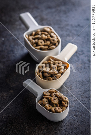 Dry kibble pet food. Dog or cat food in scoop on black table. Dry kibble pet food. Dog or cat food in scoop on black table. 135779933