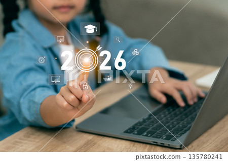 Little girl pointing at 2026 target icon on laptop for future education goals. Child setting success objectives with digital technology, innovation, and online learning icons. 135780241