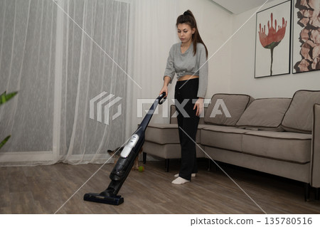 Woman Vacuums the Floor in the Living Room of Her Modern Home 135780516