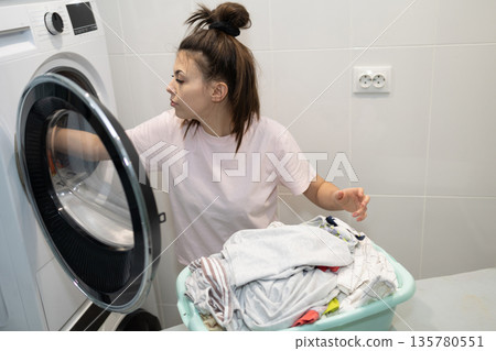 Woman Doing Laundry in a Home Laundry Room During the Day While Sorting Clothes in a Basket 135780551