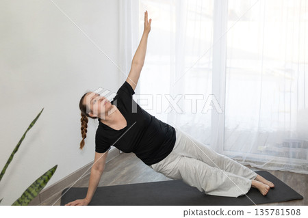 Woman Practices Yoga in Sunny Room With White Curtains and Indoor Plant 135781508