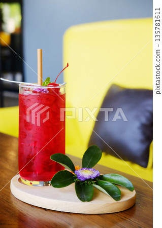 A glass of red soda with a cherry and violet flower decorated on topping on wwoden table A glass of red soda with a cherry and violet flower decorated on topping on wwoden table 135781611