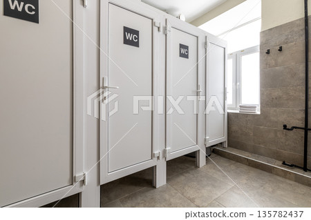 Row of modern white toilet stalls in a shared hostel bathroom 135782437
