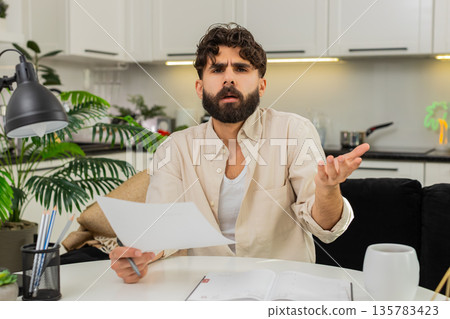 Indian man reading official letter facepalm stressed about finances writing action plan in notebook Indian man reading official letter facepalm stressed about finances writing action plan in notebook 135783423