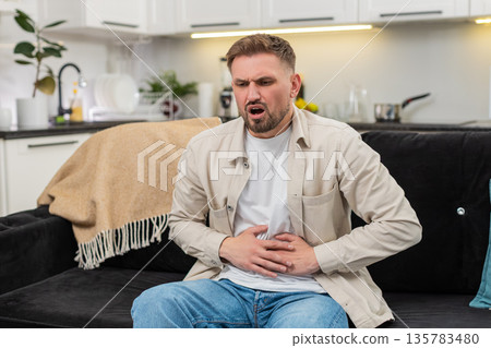 Young man presses hands to stomach cramps pain after heavy fatty food breath control pause routine 135783480