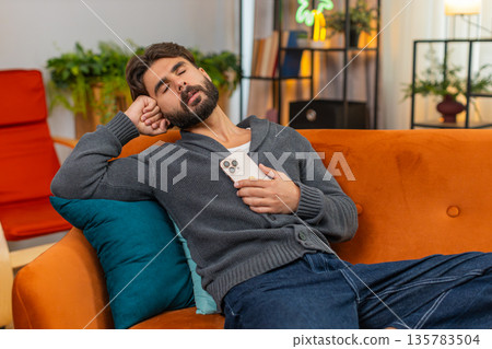 Indian man naps with smartphone wakes to loud alert important message quick look startled reaction Indian man naps with smartphone wakes to loud alert important message quick look startled reaction 135783504