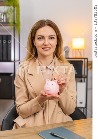 Businesswoman shakes empty piggy bank frowns drops coin inside makes save money gesture motivated Businesswoman shakes empty piggy bank frowns drops coin inside makes save money gesture motivated 135783505