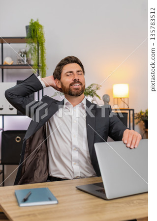 Middle-aged businessman finishes final report powers down laptop closes lid stretches smiles relaxed 135783512