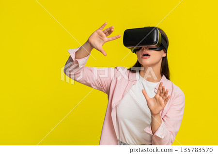 Woman wearing VR headset moving hands in air excited amazed virtual reality immersive digital world Woman wearing VR headset moving hands in air excited amazed virtual reality immersive digital world 135783570