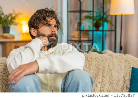 Sad frustrated young Indian man sitting at home looks pensive thinks over lonely life problems Sad frustrated young Indian man sitting at home looks pensive thinks over lonely life problems 135783857